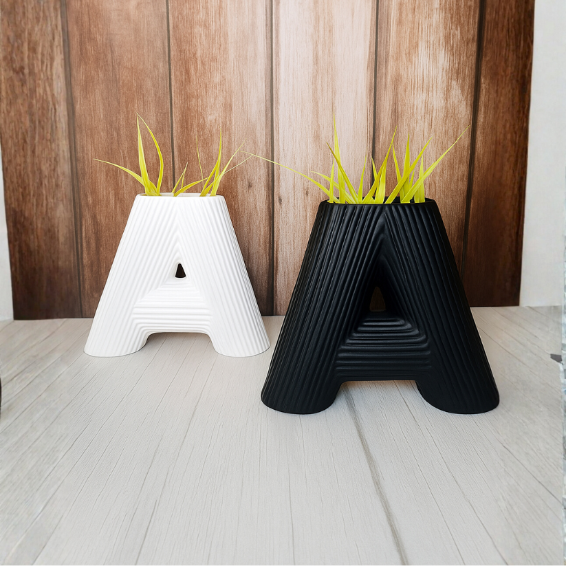 Two letter 'A' shaped planters, one white and one black, with grass-like plants on a wooden floor.