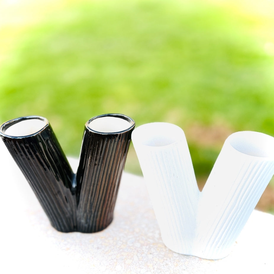 Two black and two white ribbed vases on a textured surface with a blurred green background
