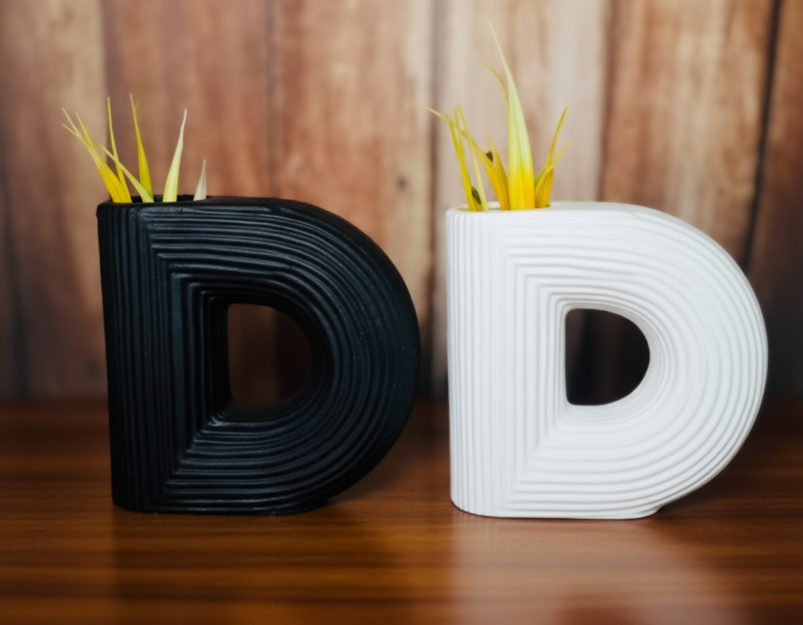 Black and white letter 'D' shaped vases with yellow sticks on a wooden surface.