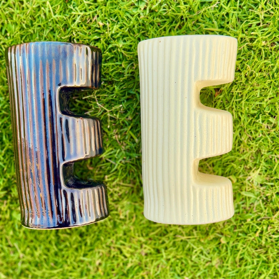 Two textured 'E' letters, one metallic and one beige, on a grass background