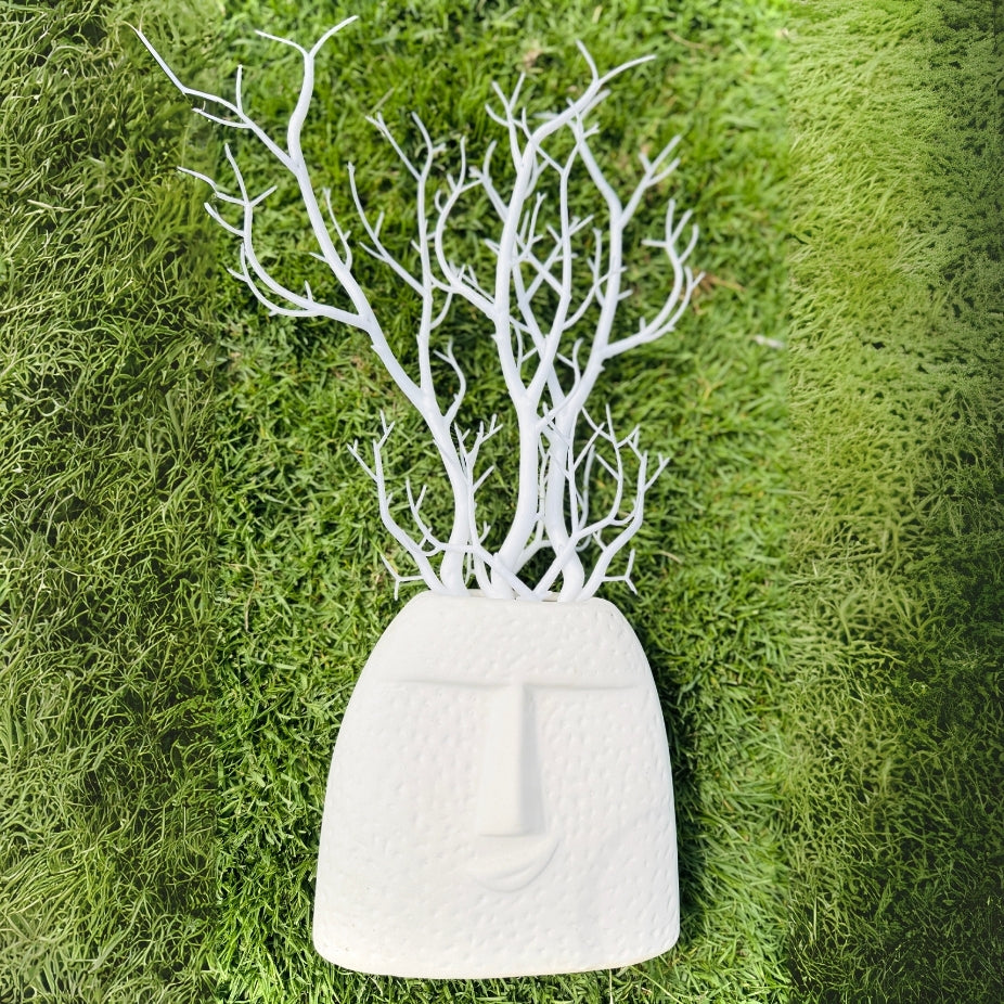 White decorative vase with branch-like structure on a green moss background