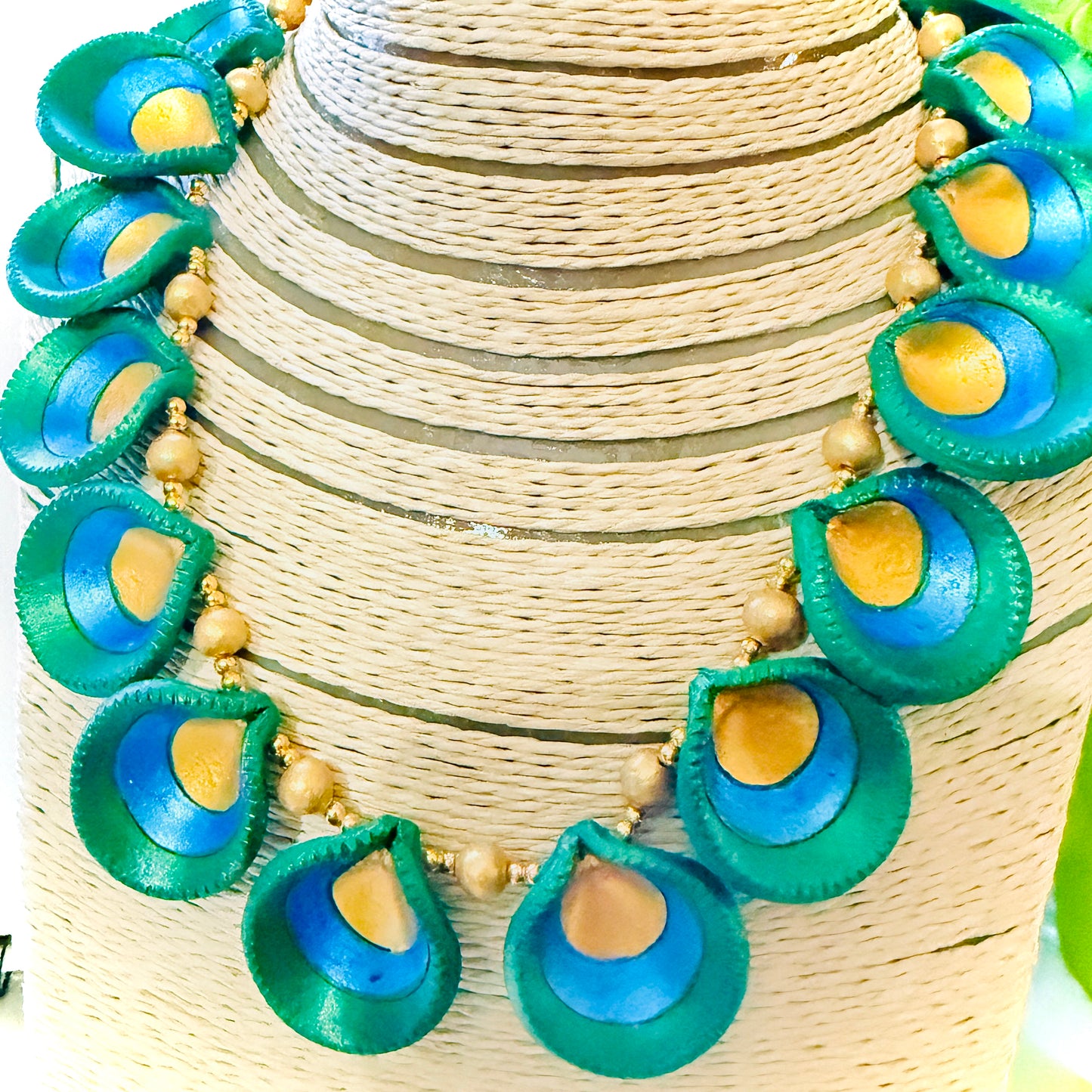 Necklace with green and blue peacock feather-like pendants on a woven surface