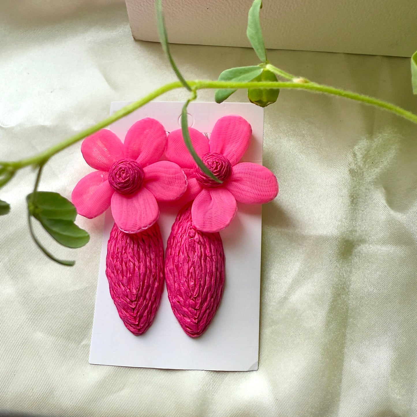 Pink floral earrings on a white card with green leaves in the background
