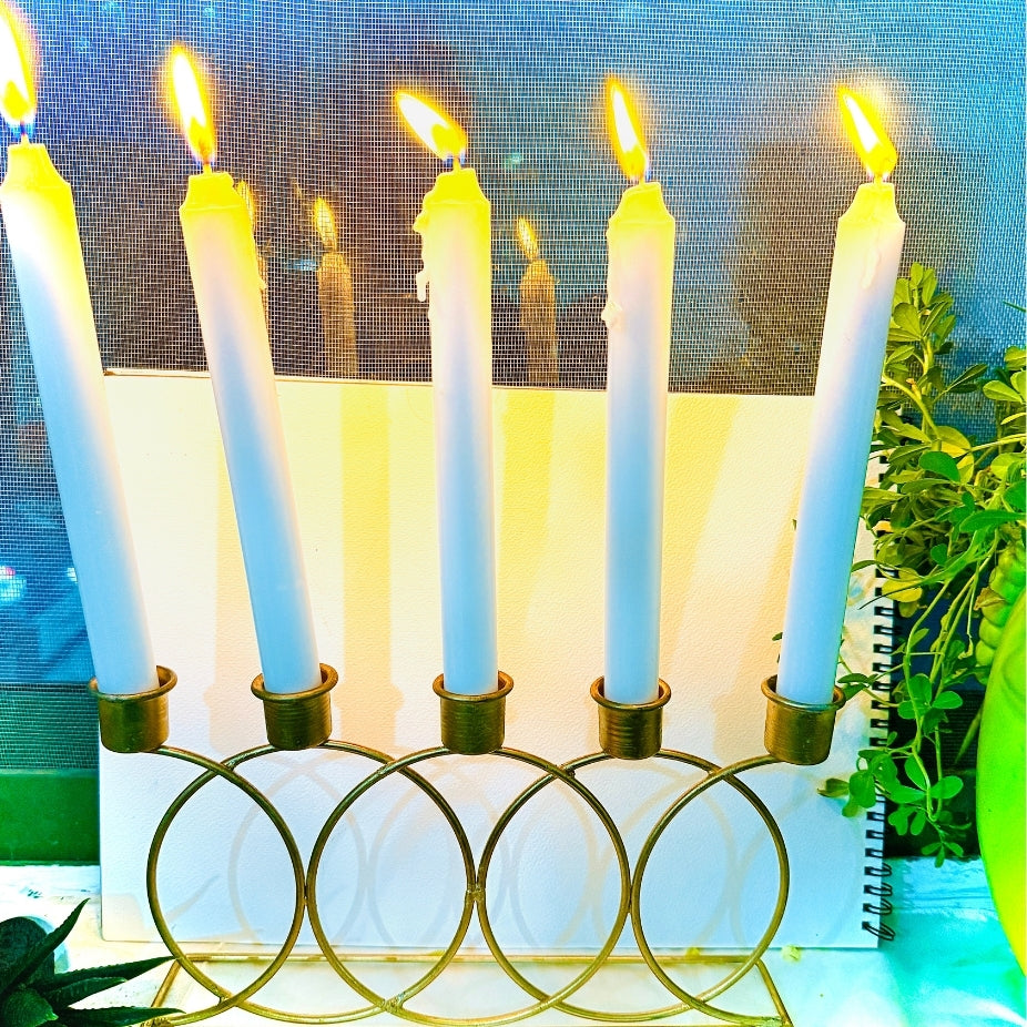 Candle holder with lit candles on a table with a plant and notebook in the background