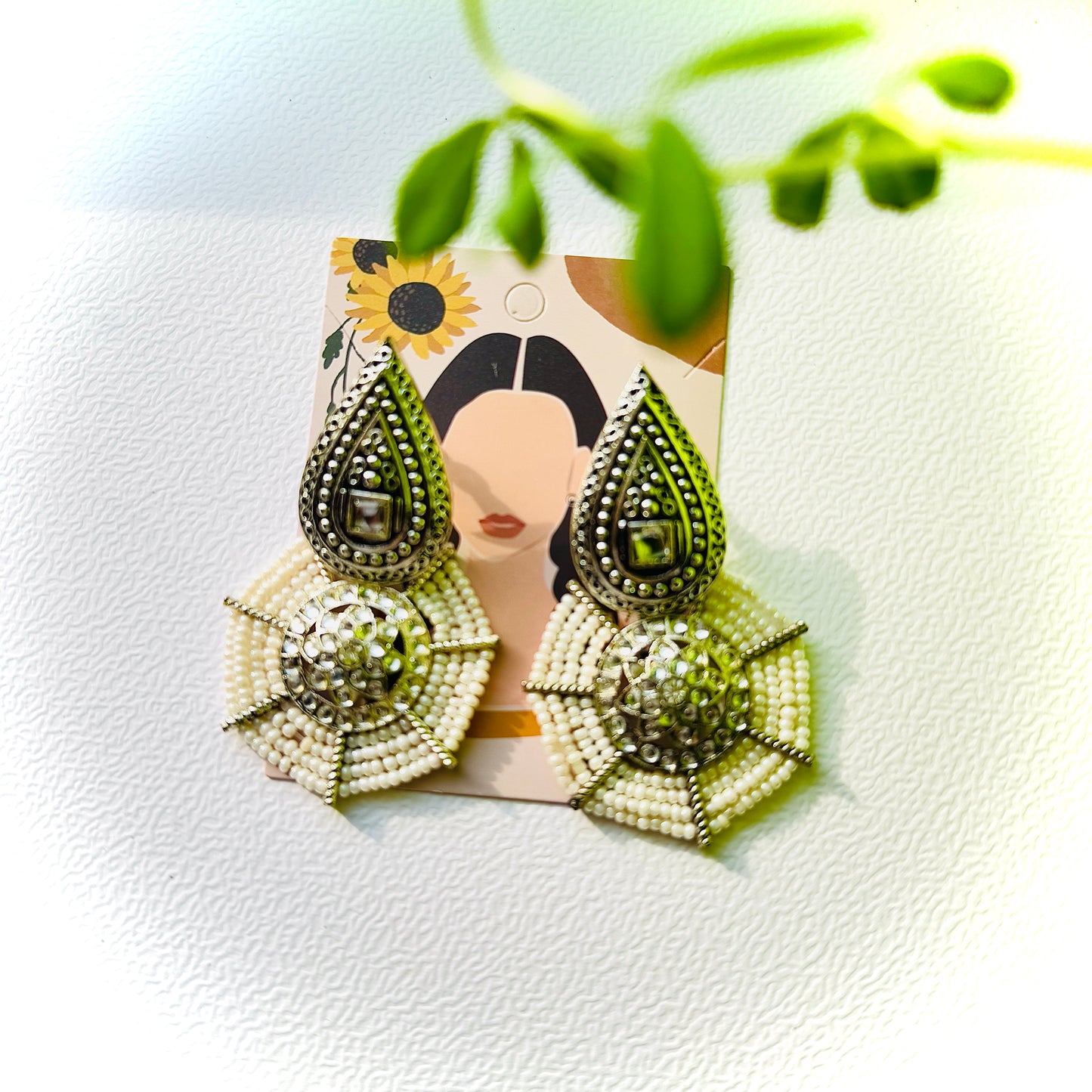 Pair of beaded earrings on a decorative card with a plant in the background