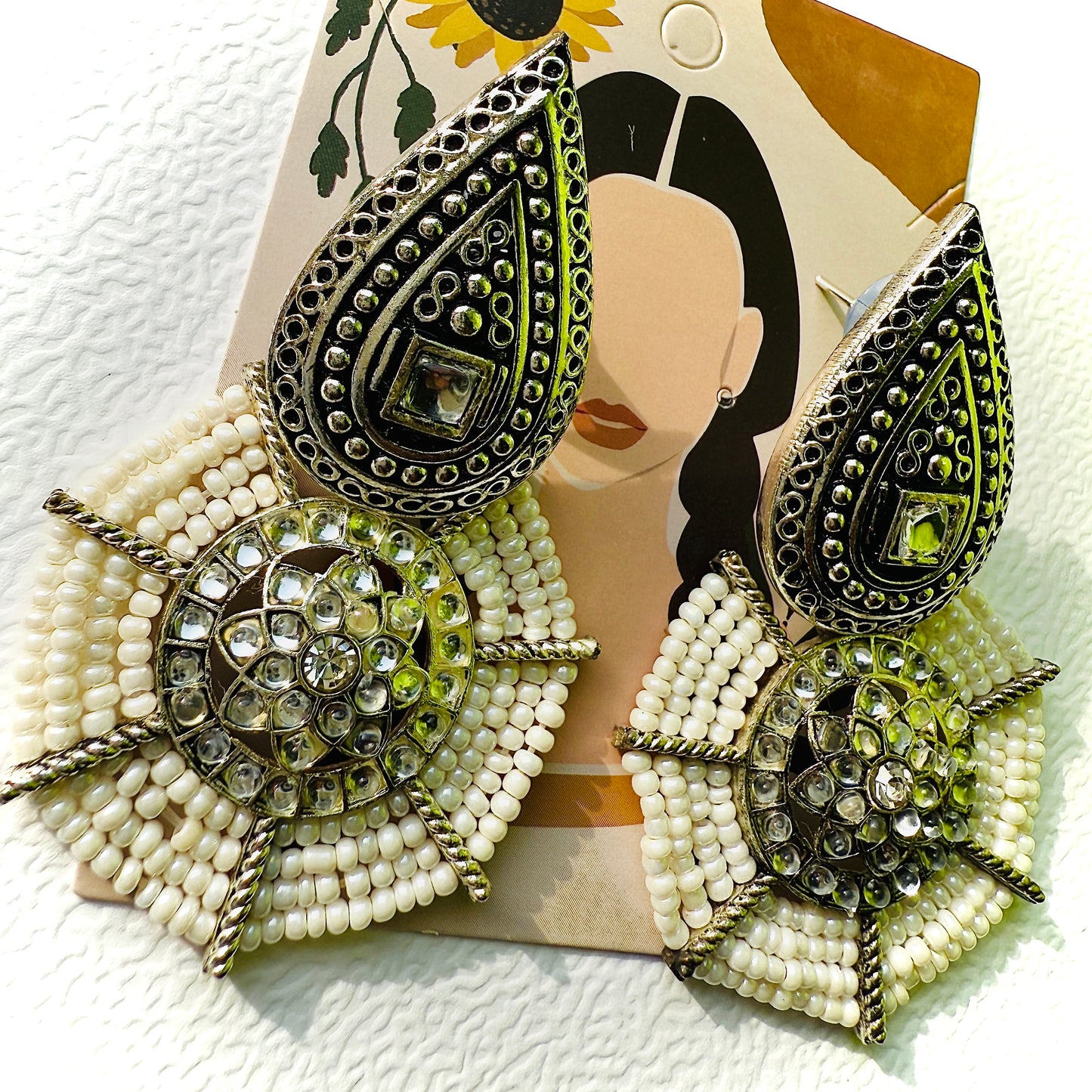 Decorative earrings with beads and metallic accents on a card with a face design.