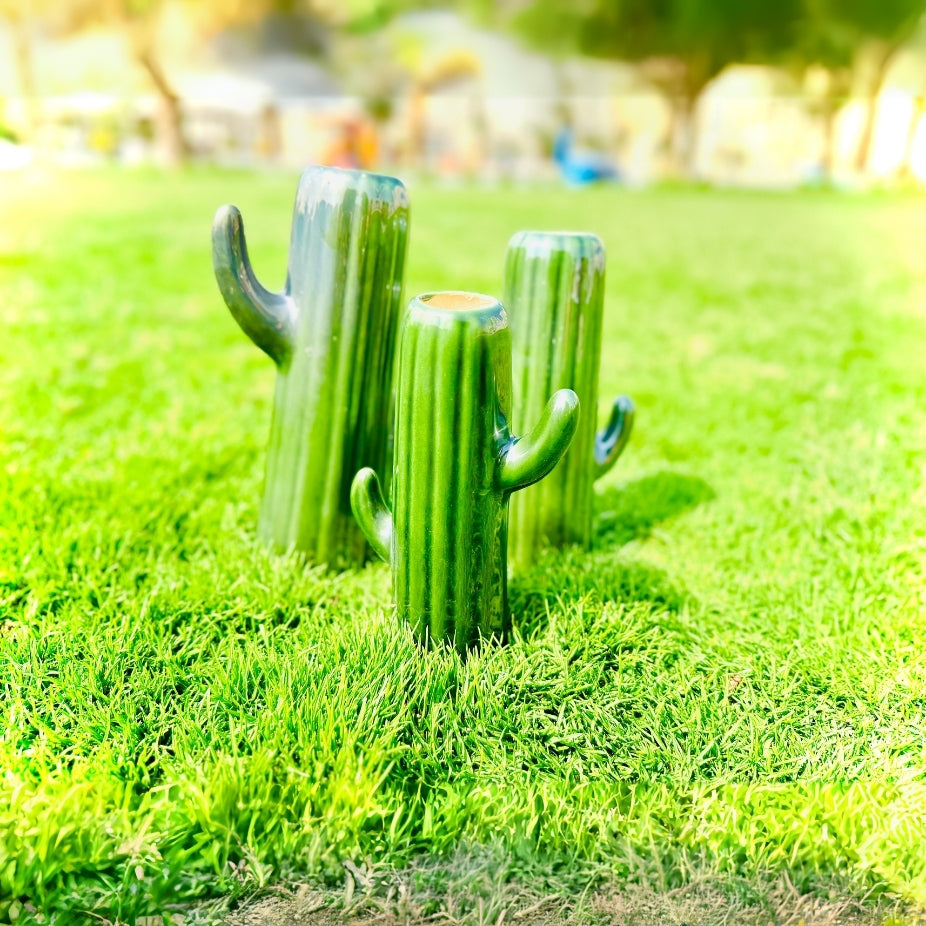 Three cactus-shaped glasses on a grassy field with a blurred background