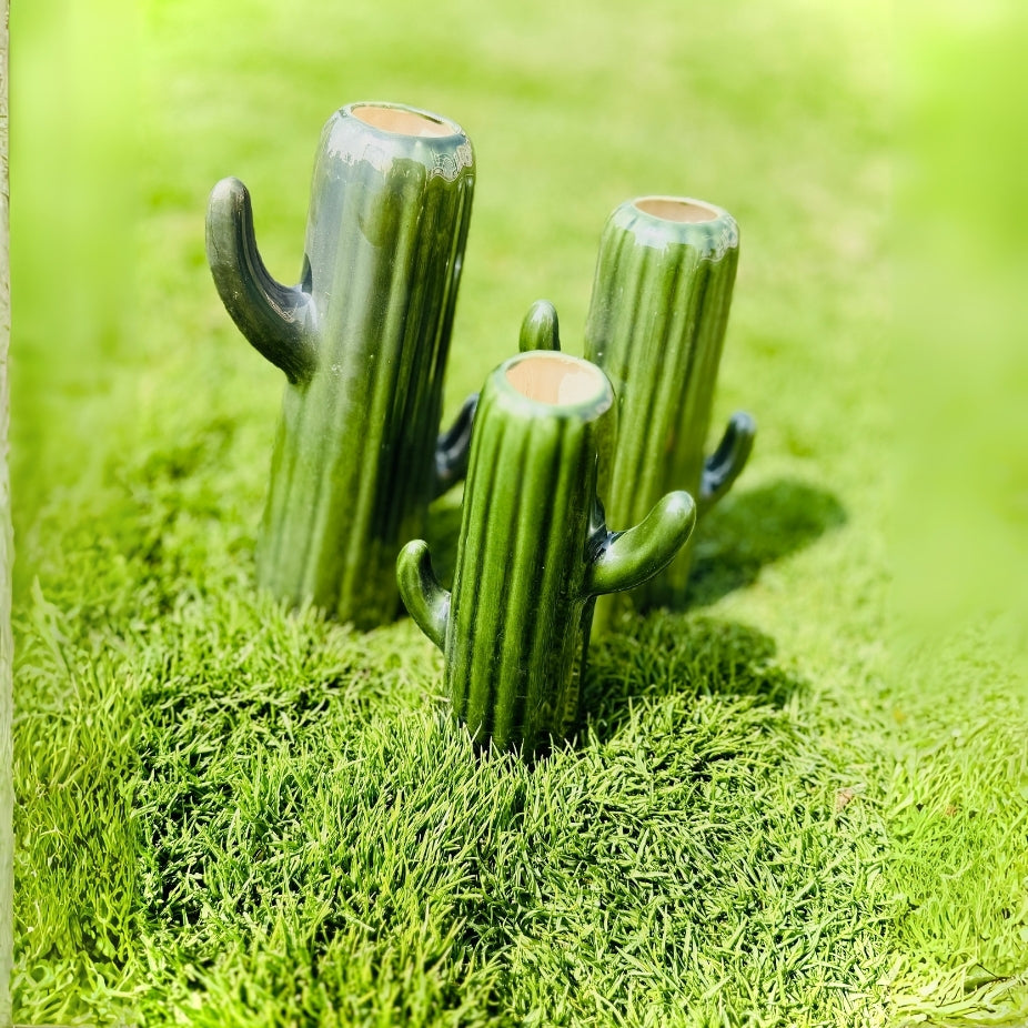 Three green cactus-shaped candles on a bed of artificial grass with a blurred green background