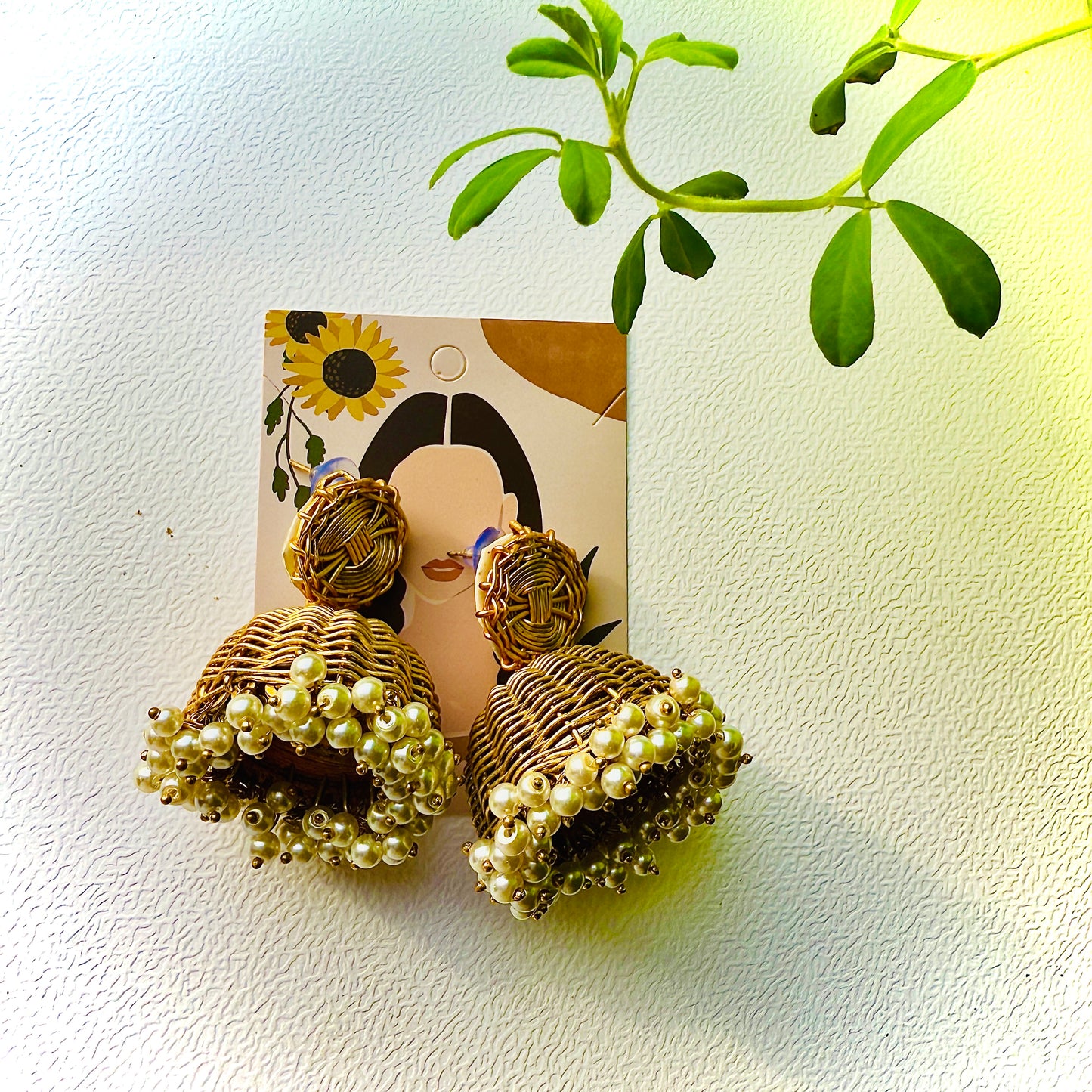 Pair of gold earrings with pearl-like beads on a white background with a plant leaf.