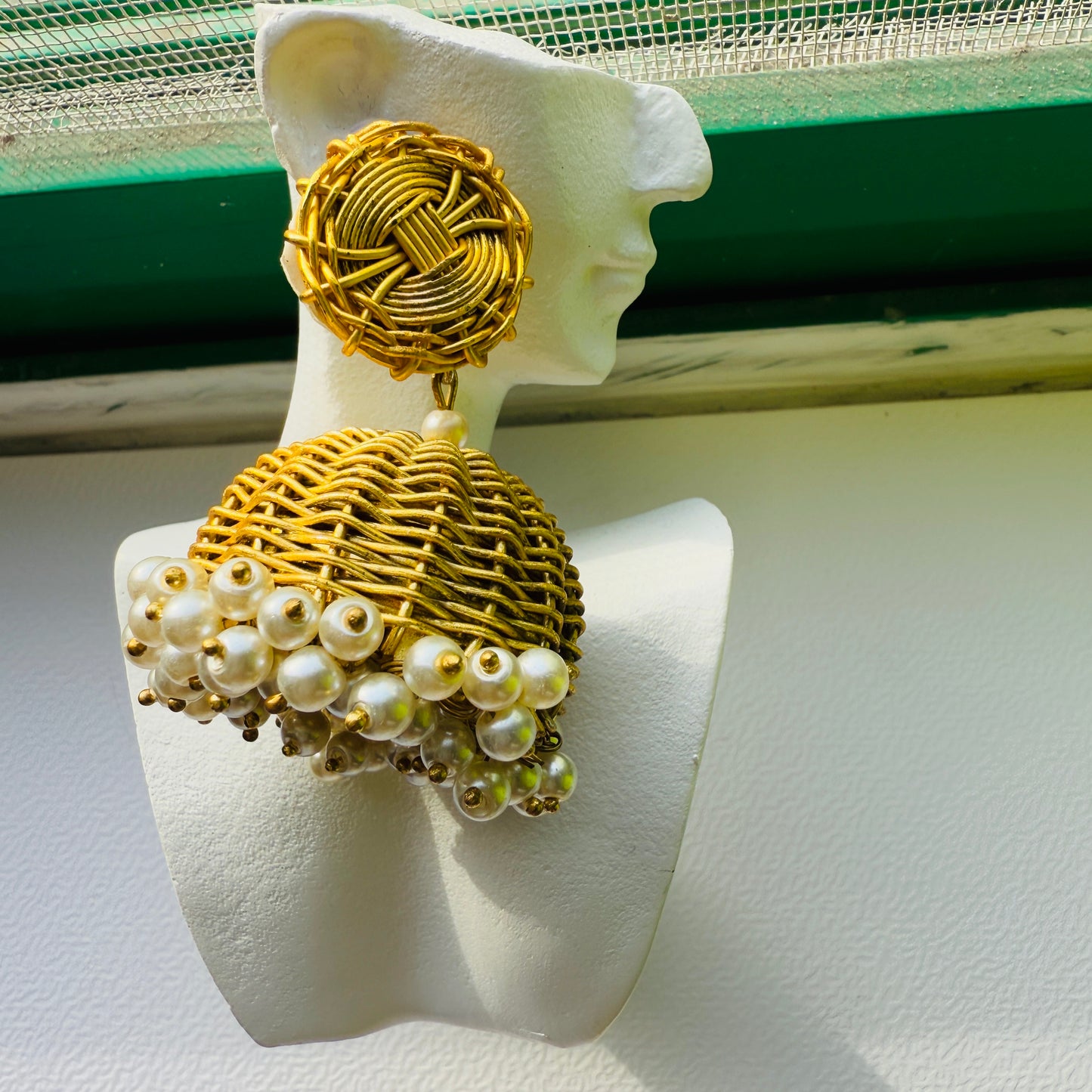Gold and pearl earrings on a mannequin bust against a white background