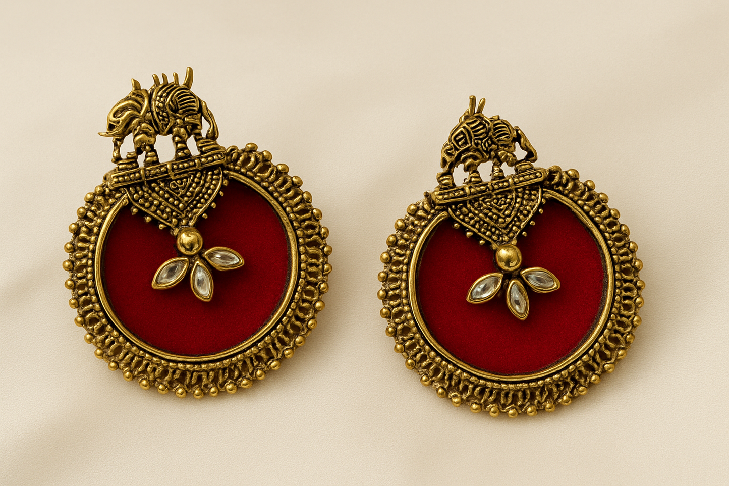 Pair of ornate earrings with red center and gold frame on beige background