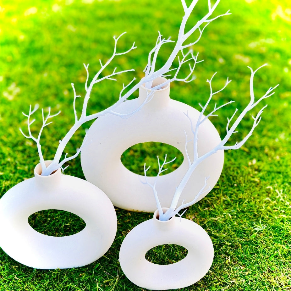 Set of three white circular vases with branches on a grassy background