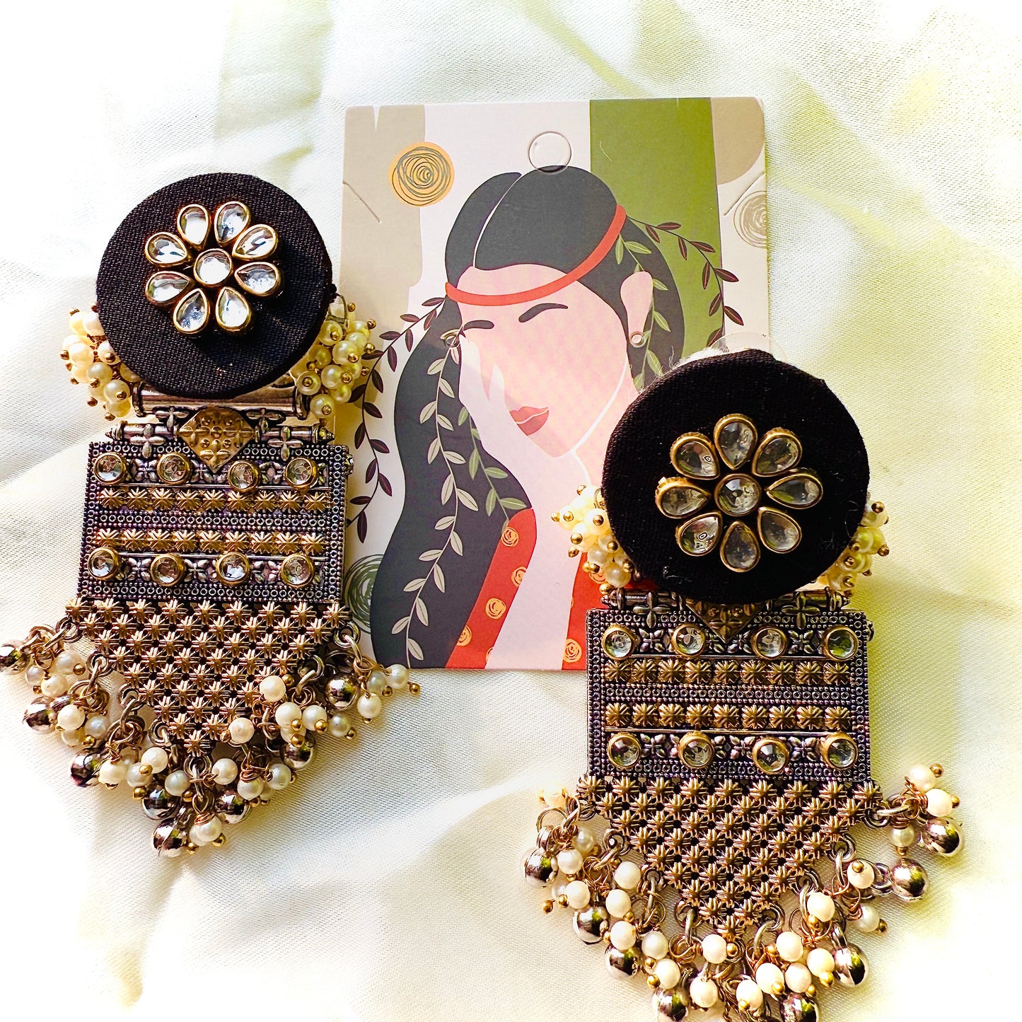 Ornate earrings with black and gold details on a white fabric background