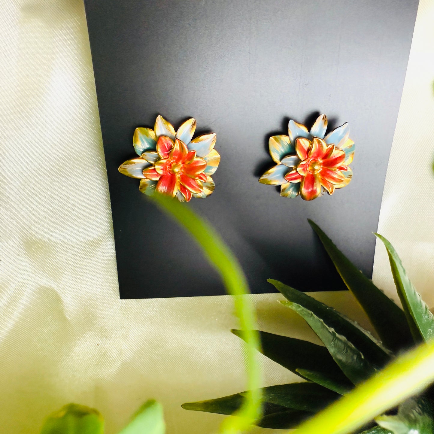 Floral earrings on a black card with green leaves in the foreground