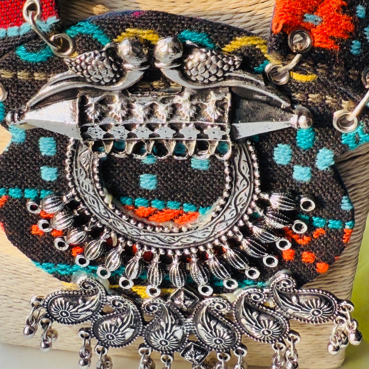 Decorative brooch with intricate silver design and colorful beads on a textured surface