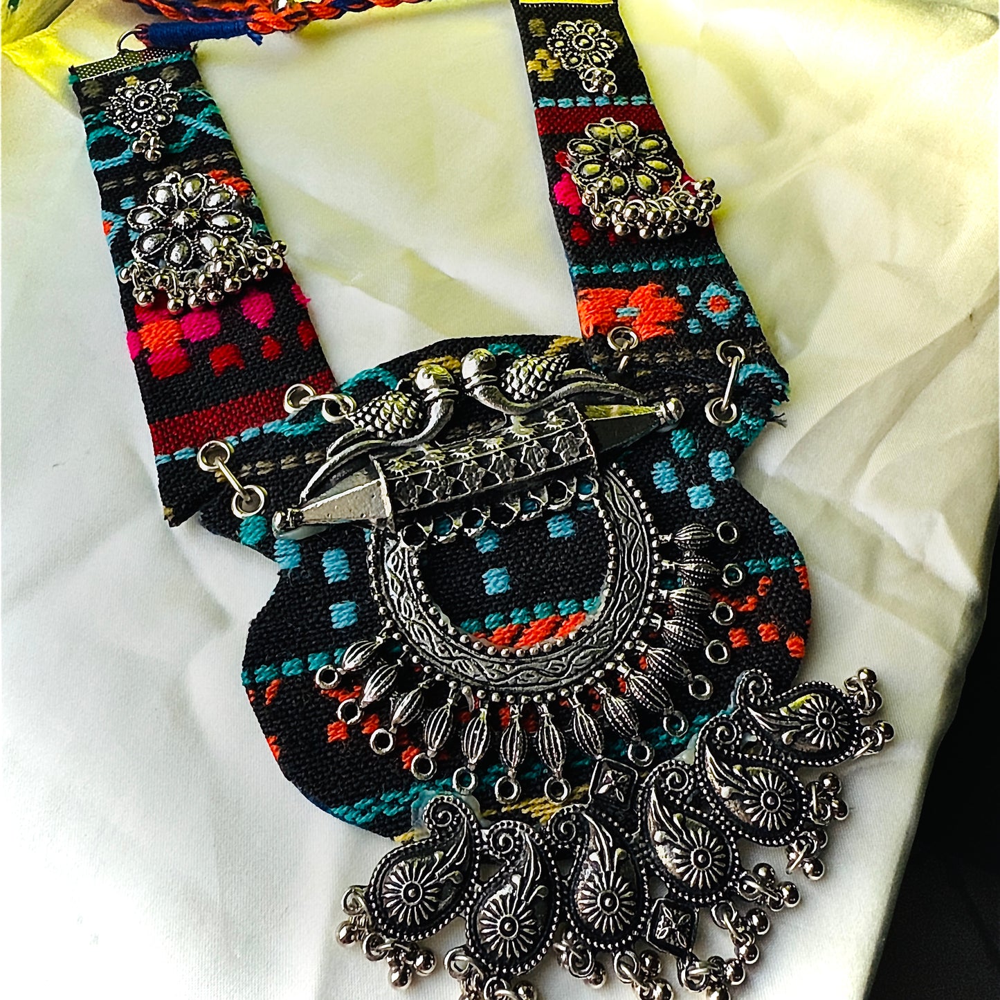 Decorative belt with intricate silver designs and colorful patterns on a white fabric background