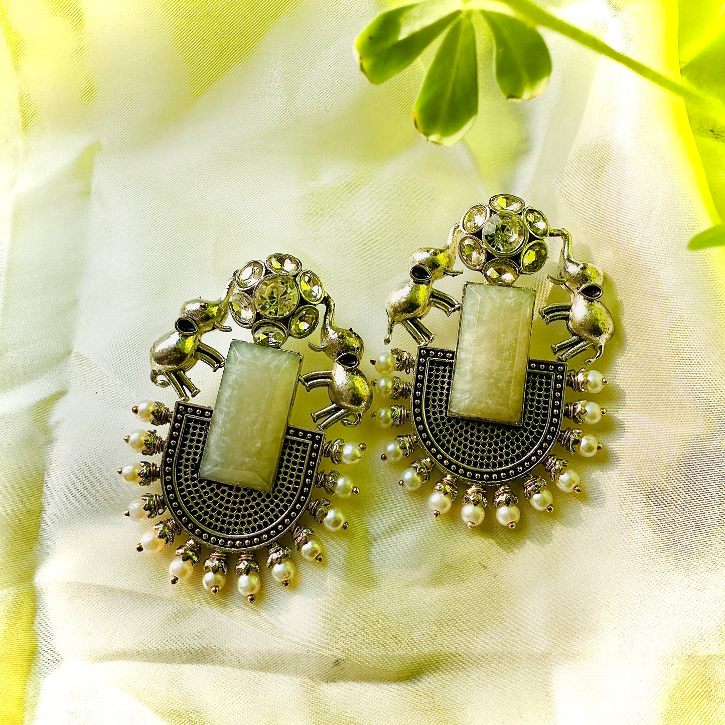 Pair of ornate earrings with green stones on a light fabric background