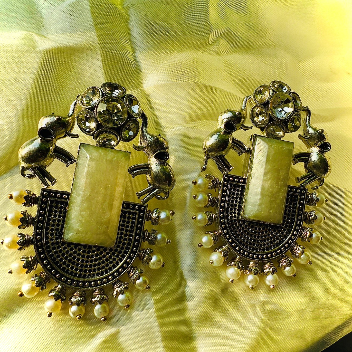 Ornate earrings with intricate designs on a yellow fabric background
