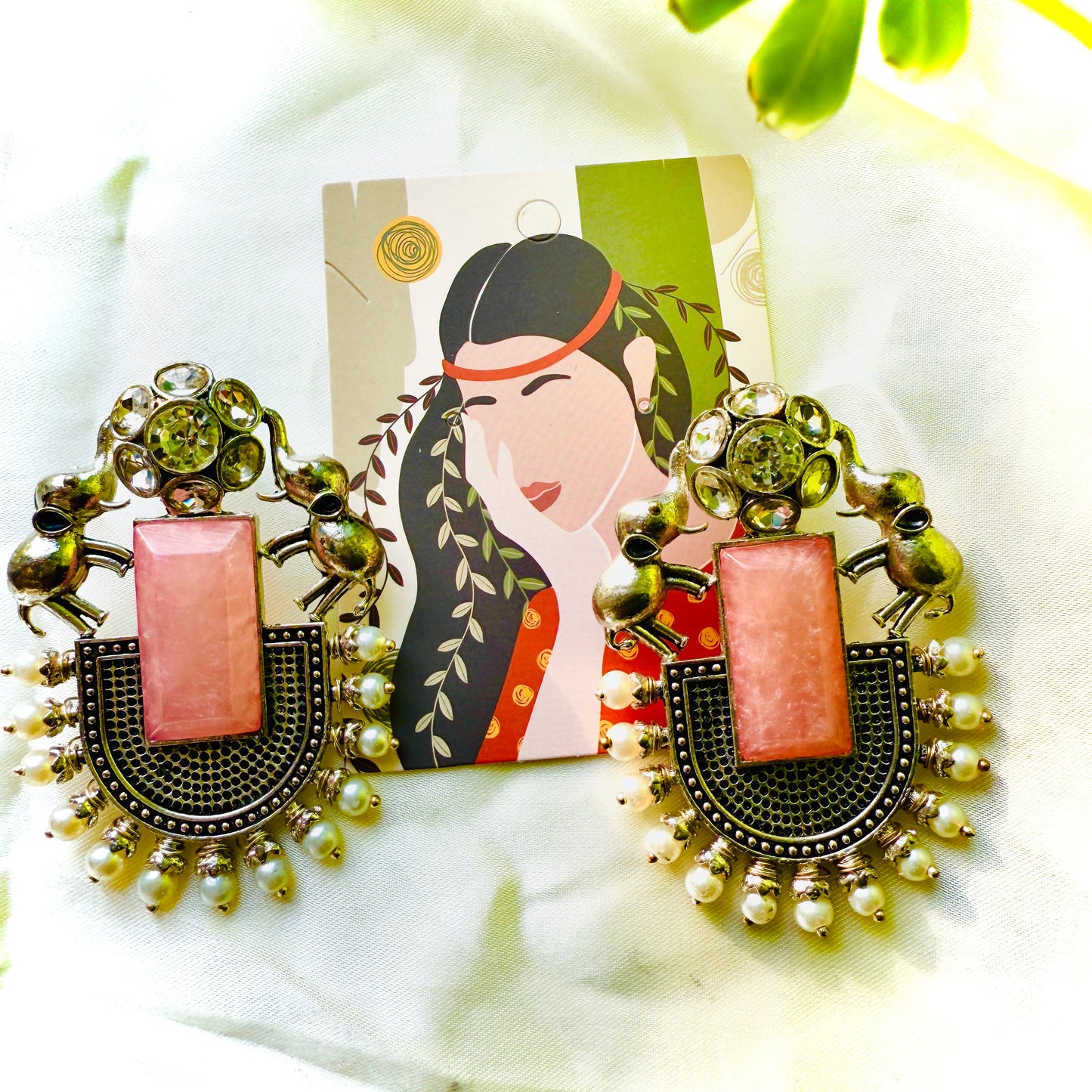 Decorative earrings with pink center and gold accents on a white surface with a decorative card.