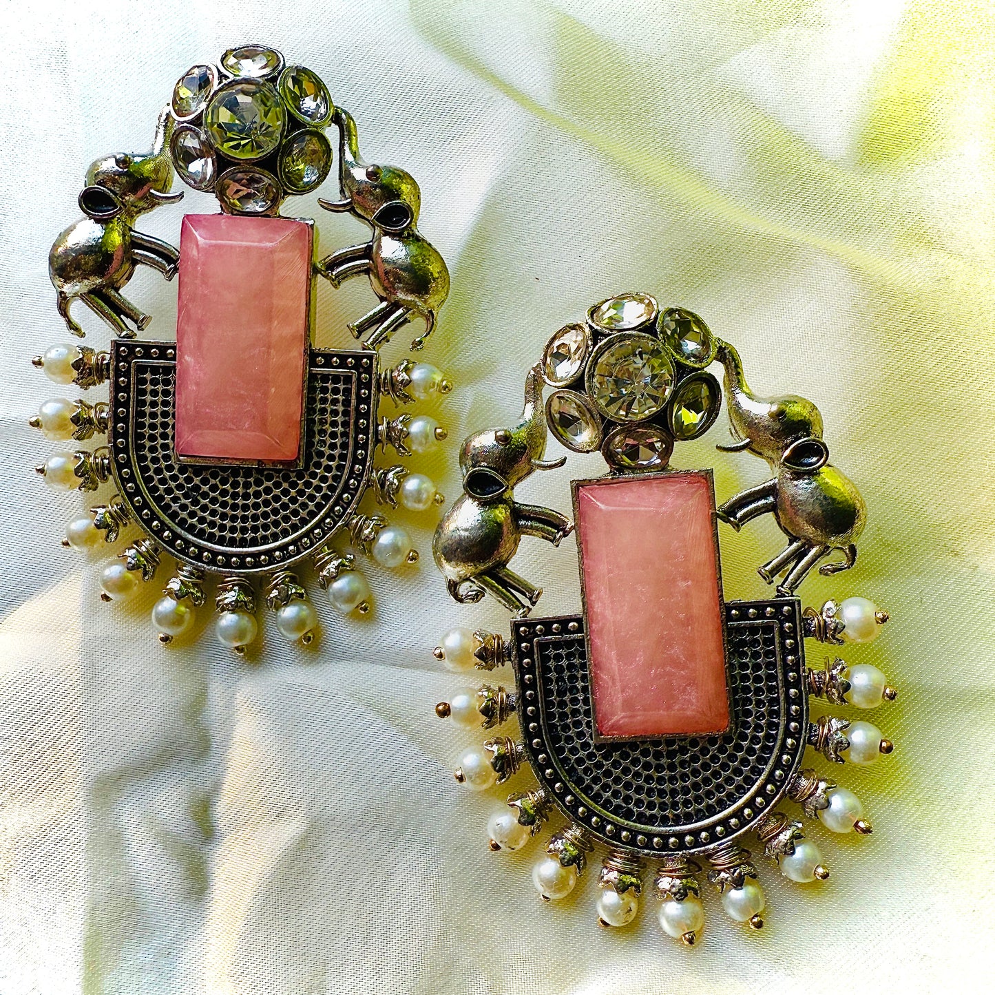 Ornate earrings with pink central stones and pearl accents on a light fabric background