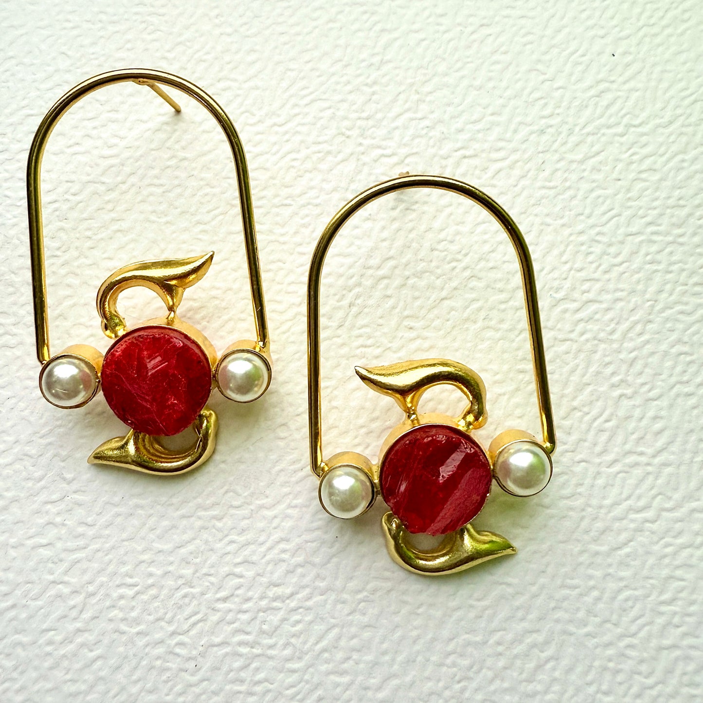 Pair of gold earrings with red stones and pearls on a textured white background