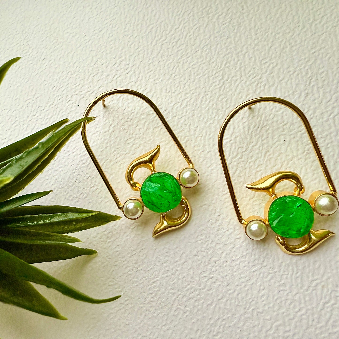 Gold earrings with green gemstones and pearls on a light background