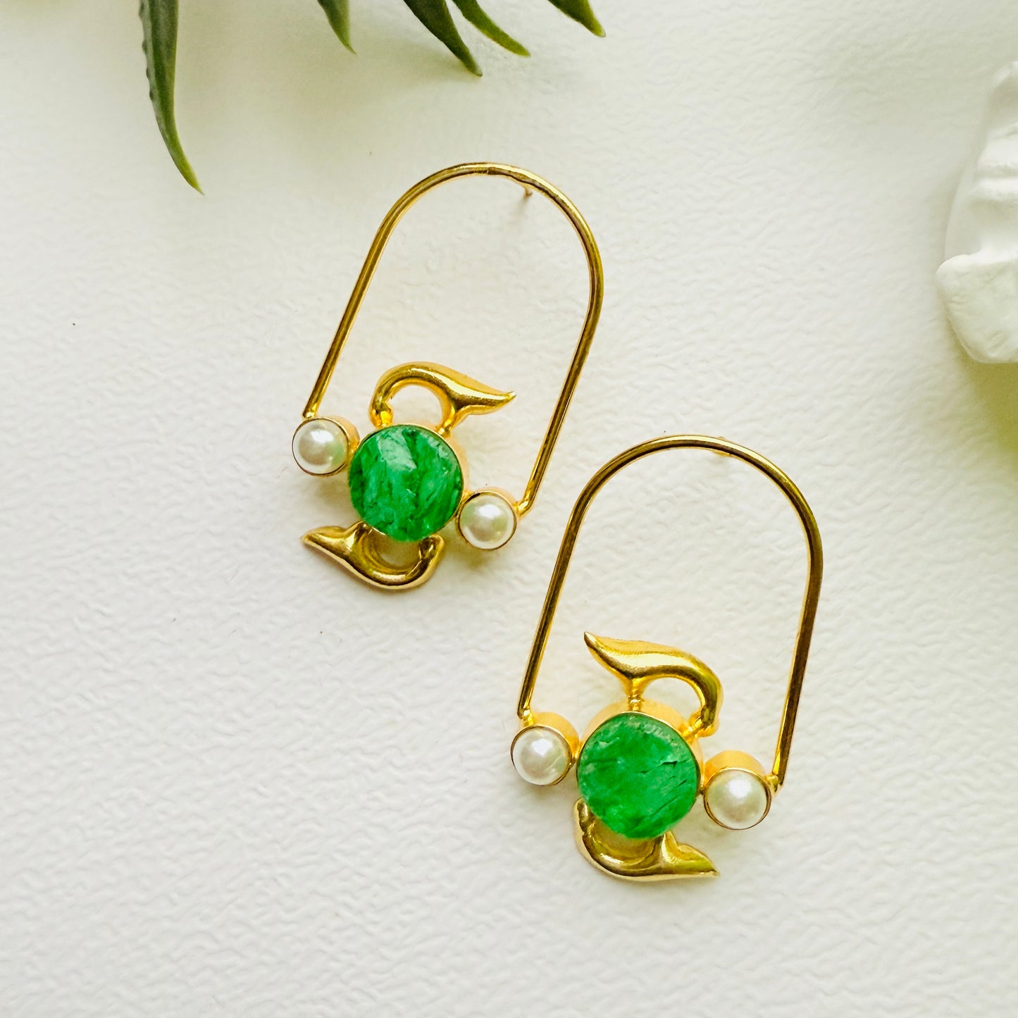 Gold earrings with green gemstones and pearls on a white surface