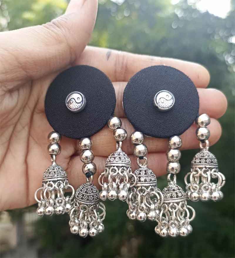 Silver earrings with black circular pads held in a hand against a blurred green background