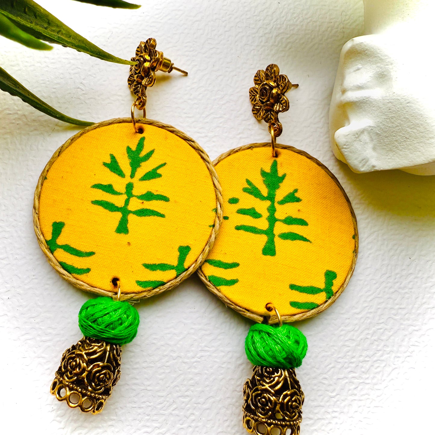 Yellow earrings with green leaf patterns and gold accents on a white background