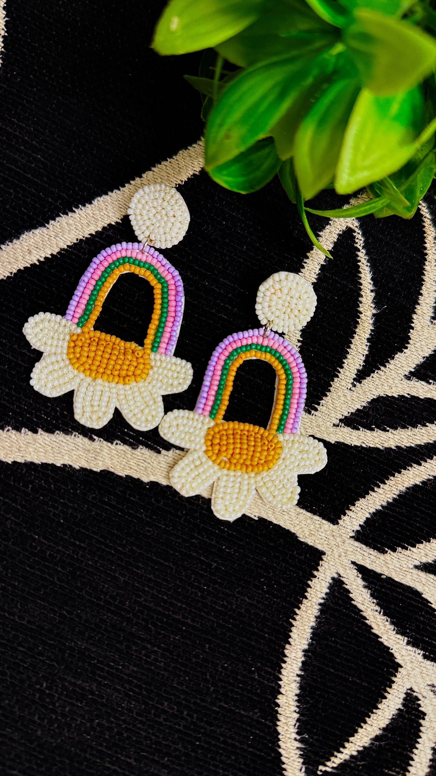 Colorful earrings with rainbow arches and white flowers on a black and beige embroidered fabric background.