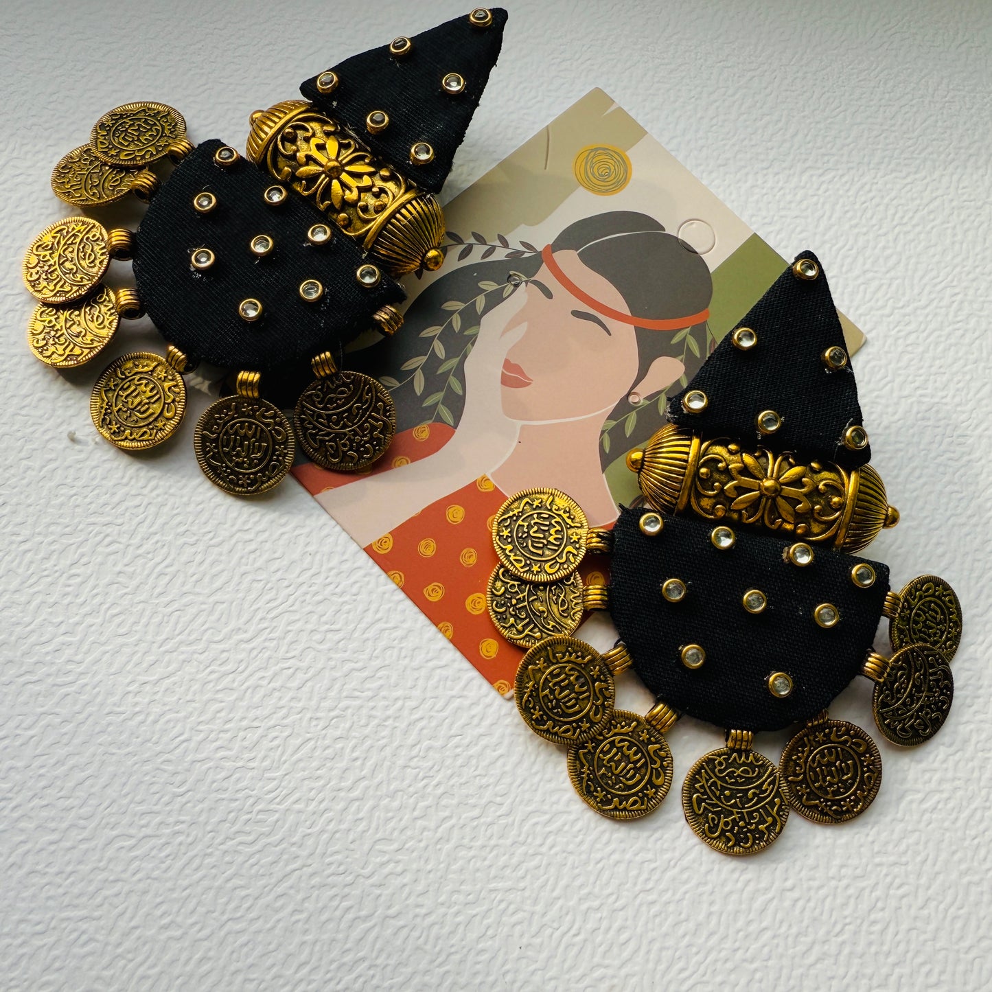 Pair of black and gold earrings on a white surface with a card featuring a woman's face.