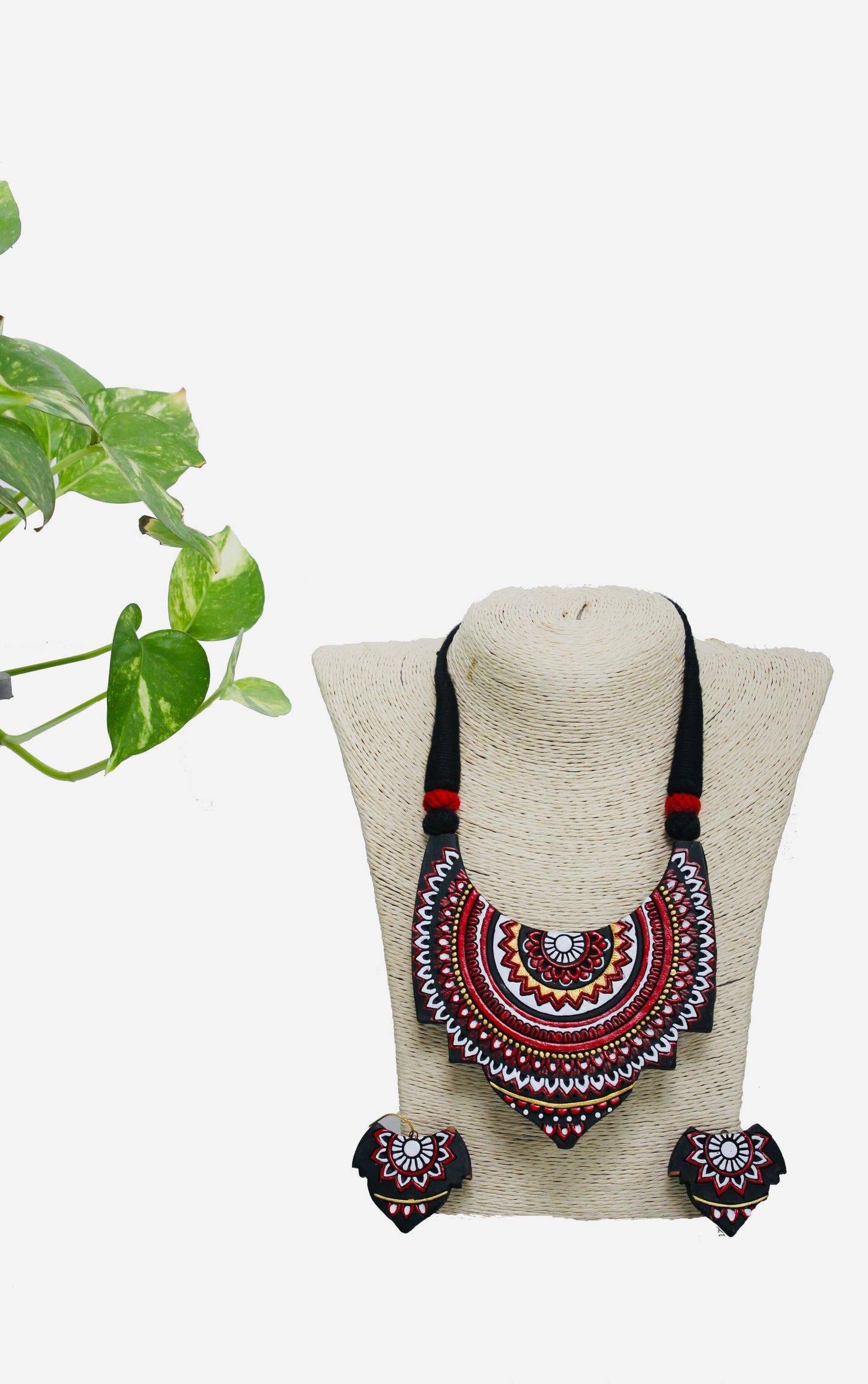Decorative necklace and earrings set on a white background with a plant on the side.