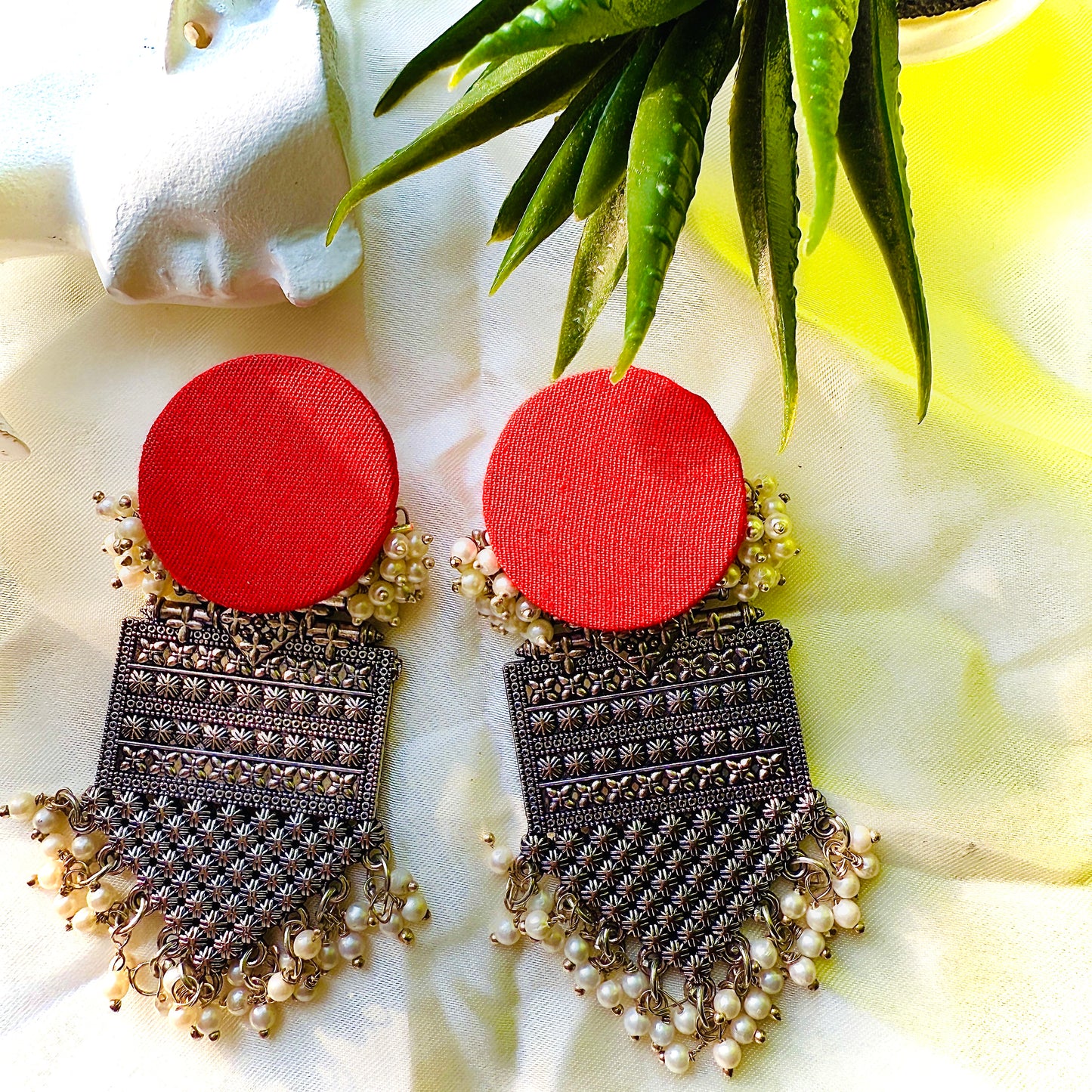 Pair of earrings with red circular tops and black and gold detailed下半部分 on a white fabric background.