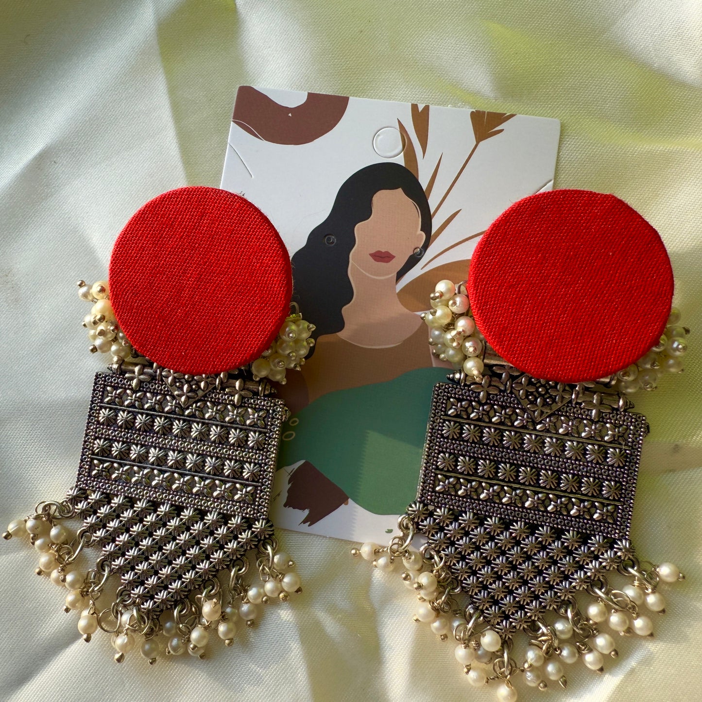 Pair of red and silver earrings with pearl details on a white background