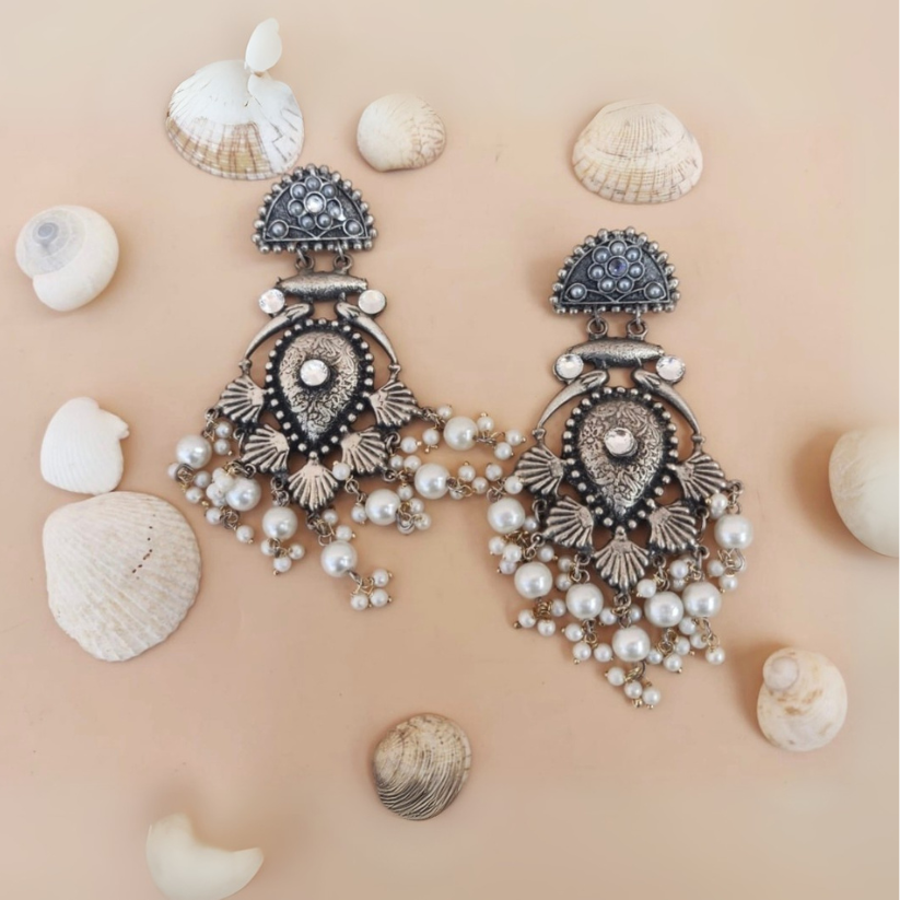 Ornate silver earrings with pearls on a beige background with seashells
