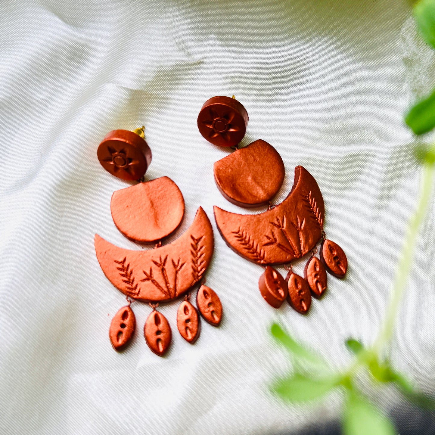 Copper-colored earrings with leaf patterns on a white fabric background