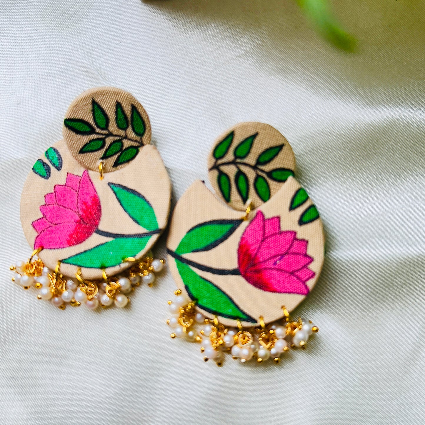 Pair of wooden earrings with floral designs and pearl-like beads on a light background