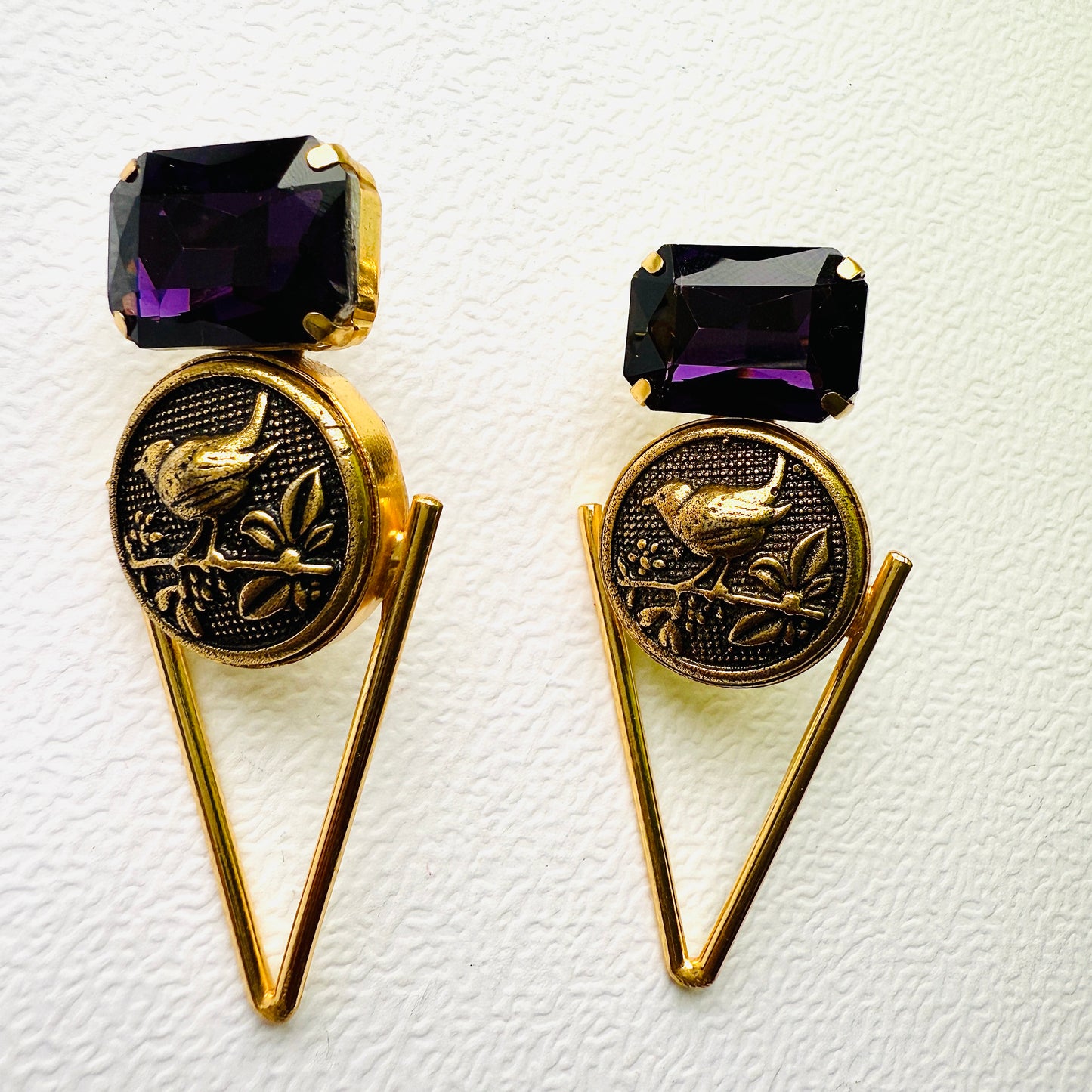 Pair of gold earrings with purple gemstones on a textured white background