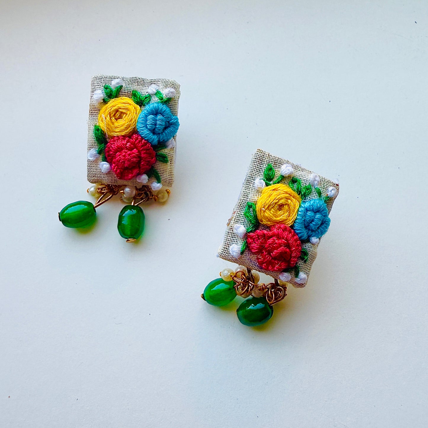 Pair of floral earrings with colorful flowers and green leaves on a white background
