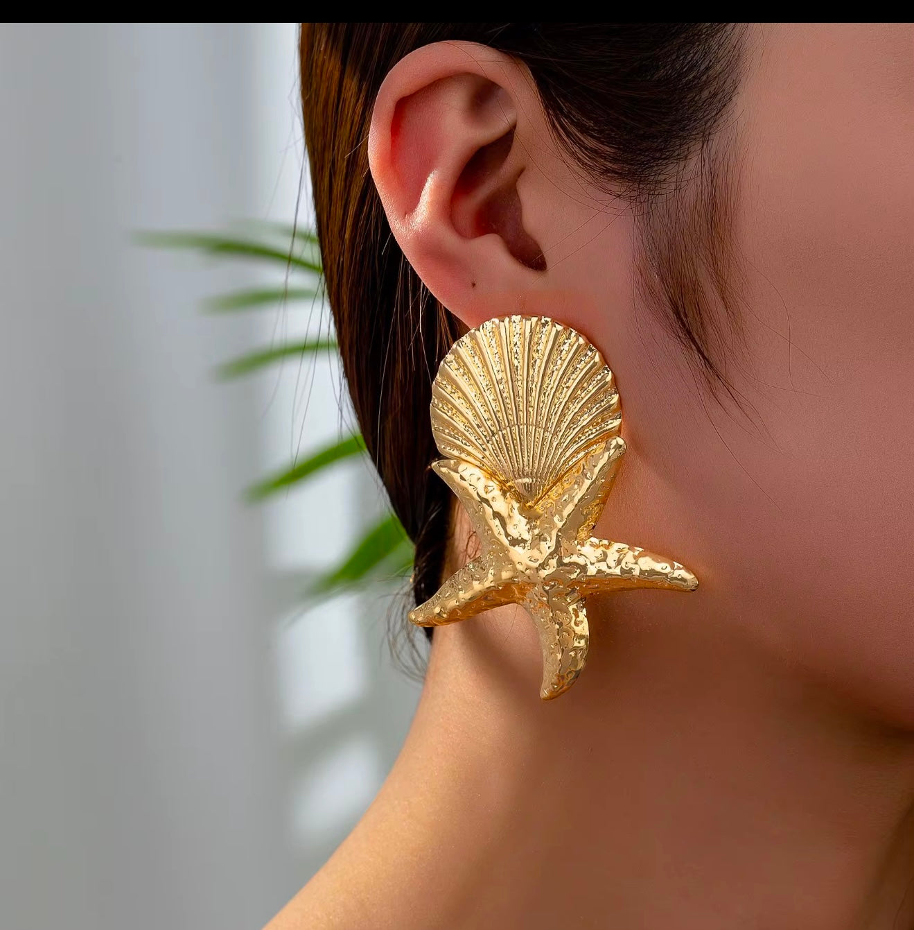 Gold shell and starfish earring worn by a person with a blurred background