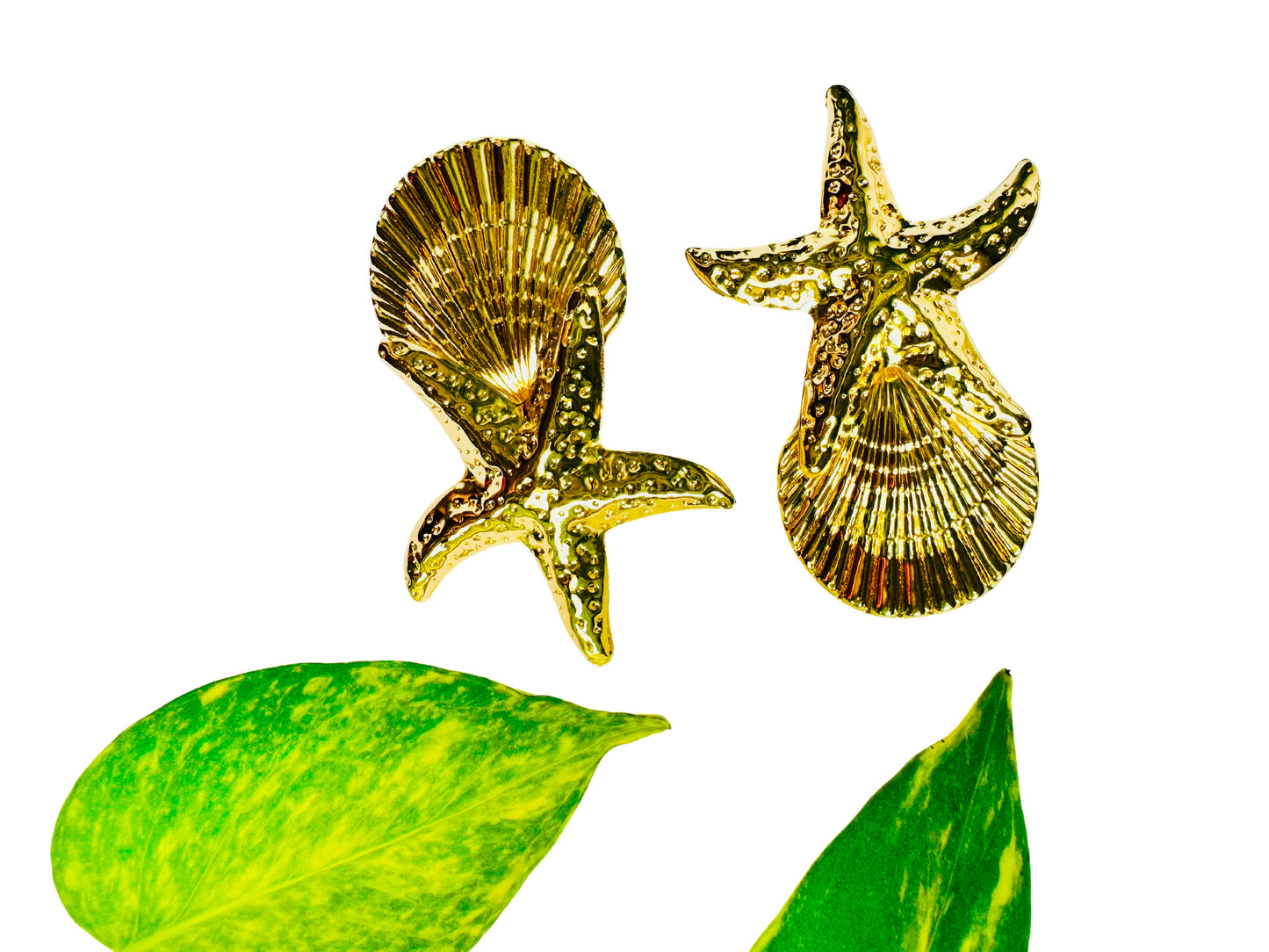 Gold starfish and shell brooches with green leaves on a white background