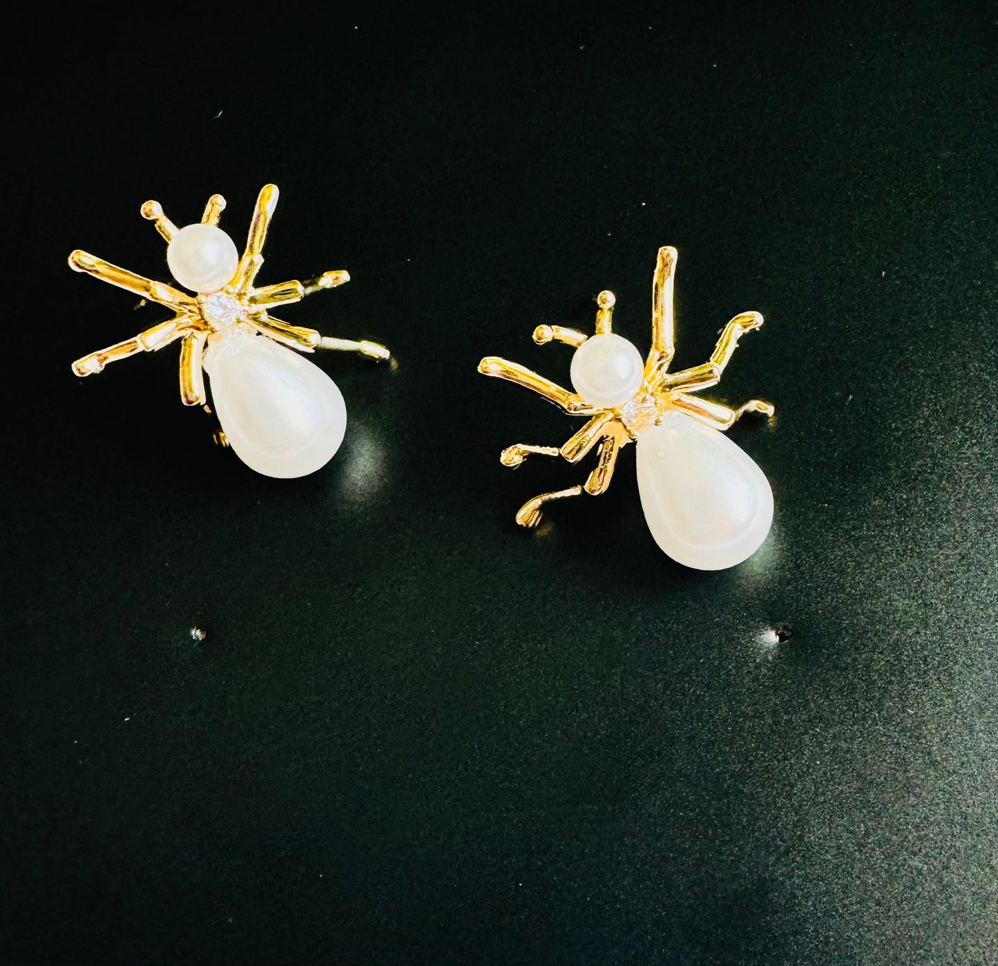 Pair of spider-shaped earrings with gold legs and white body on a black background