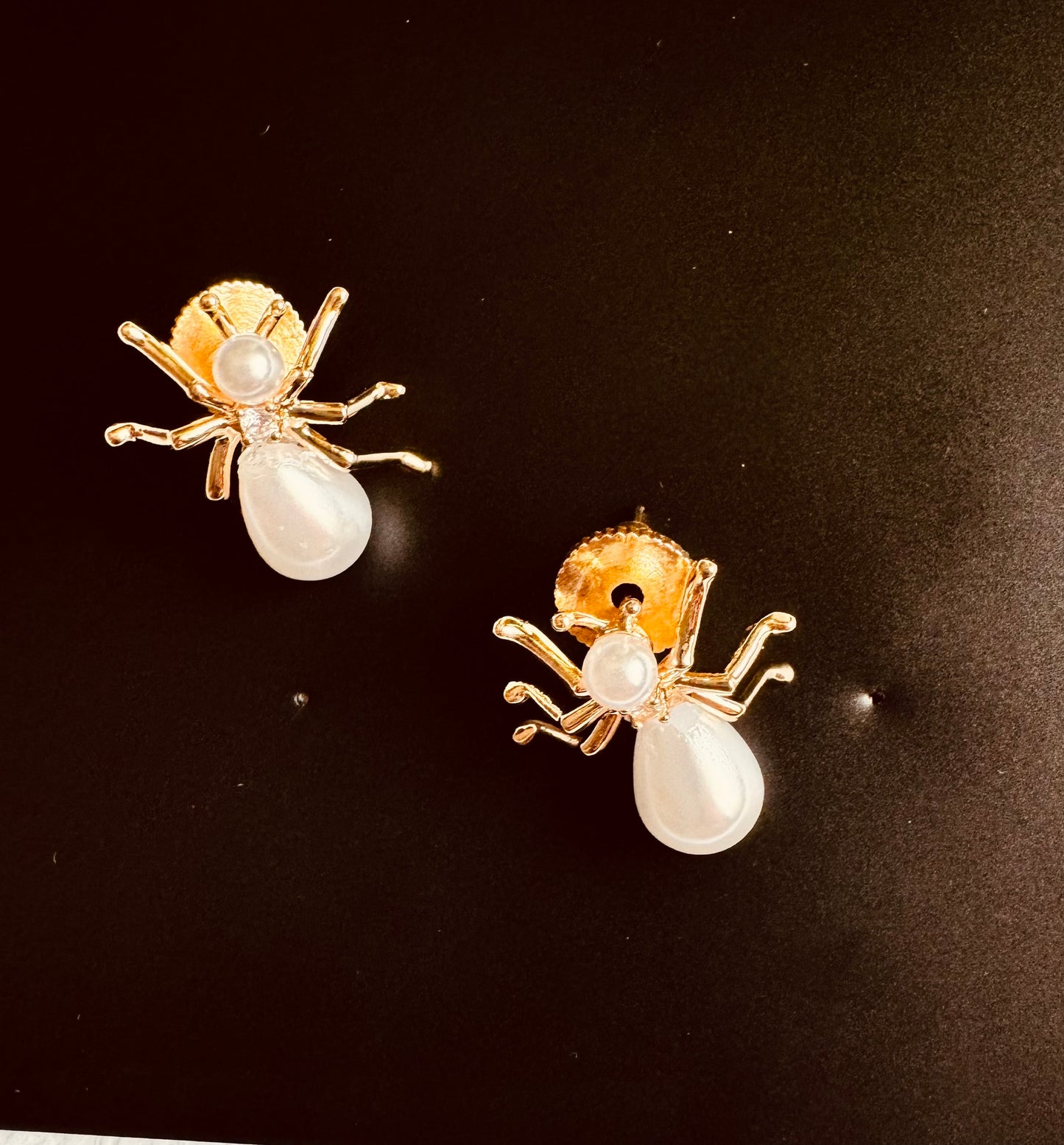 Ant-shaped earrings with gold bodies and pearl legs on a black background