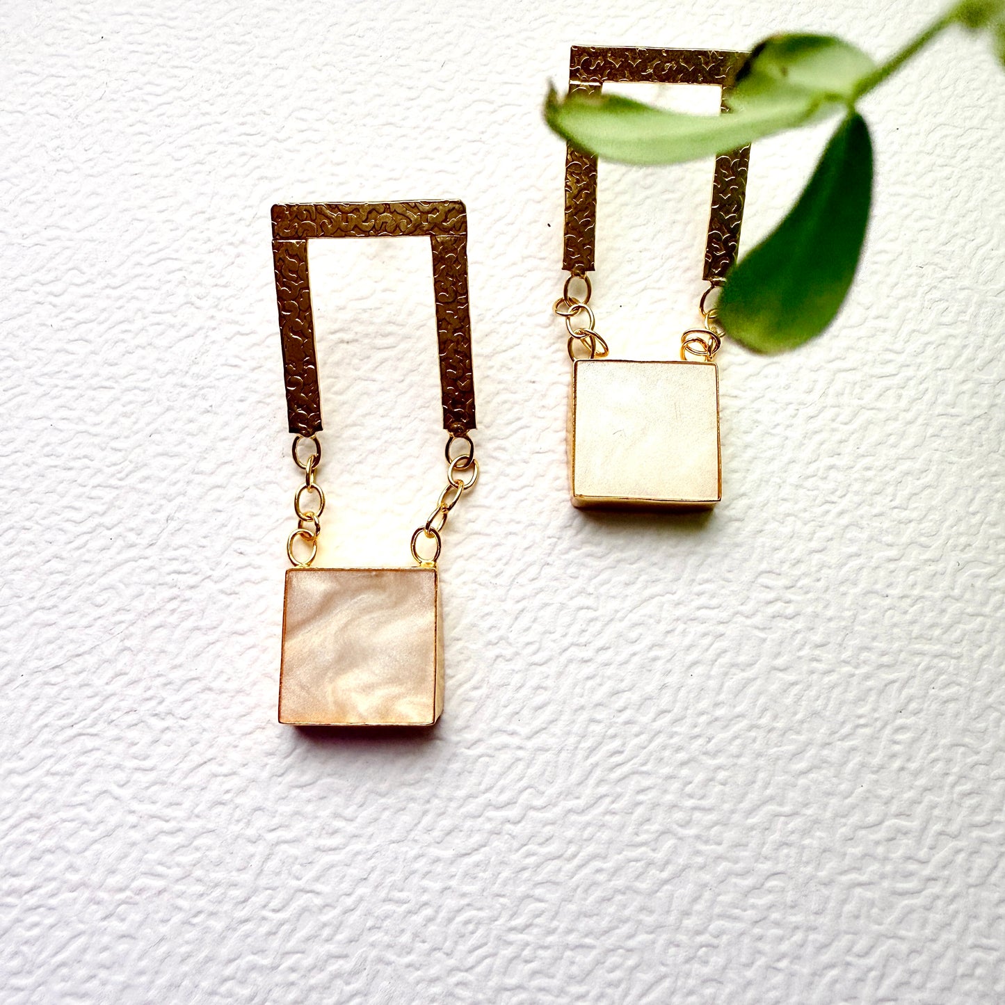 Pair of gold earrings with square pendants on a white background