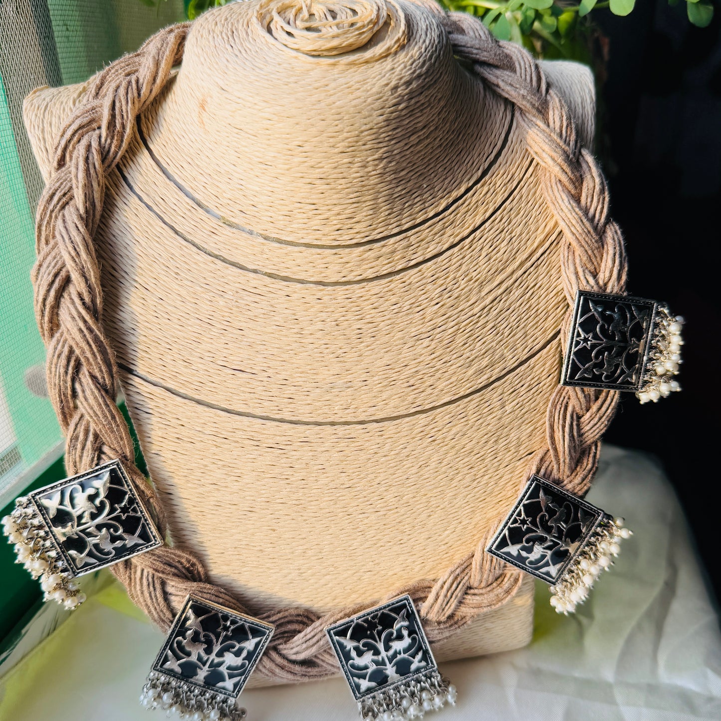Decorative earrings with intricate designs on a braided wooden stand.