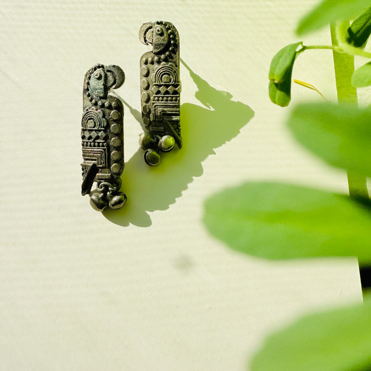 Decorative earrings on a light surface with a plant in the background