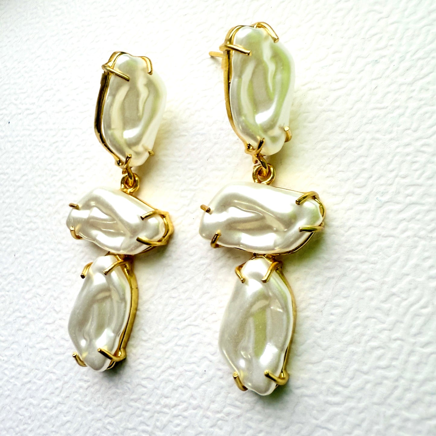 Pair of gold and white earrings on a textured white background