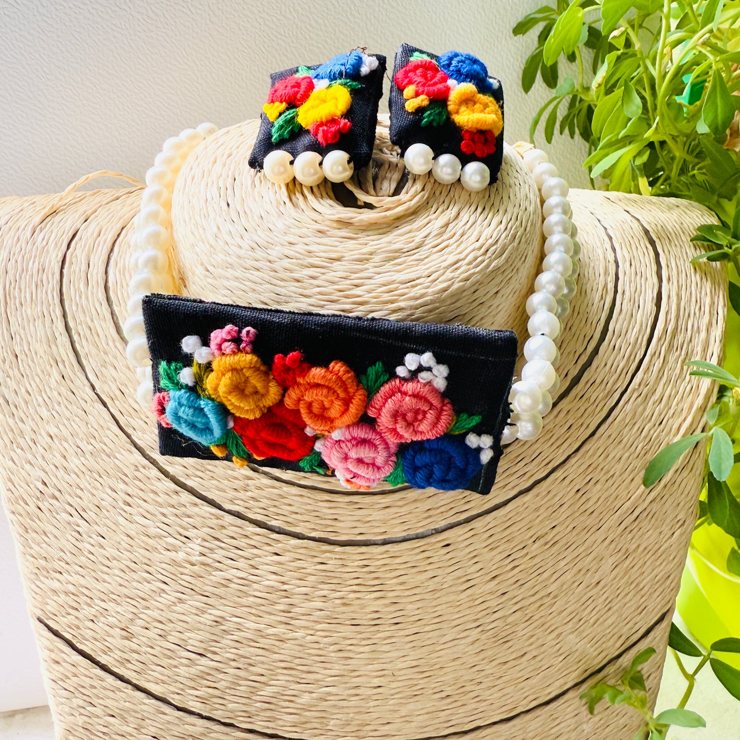 Colorful embroidered earrings on a woven hat with a plant in the background
