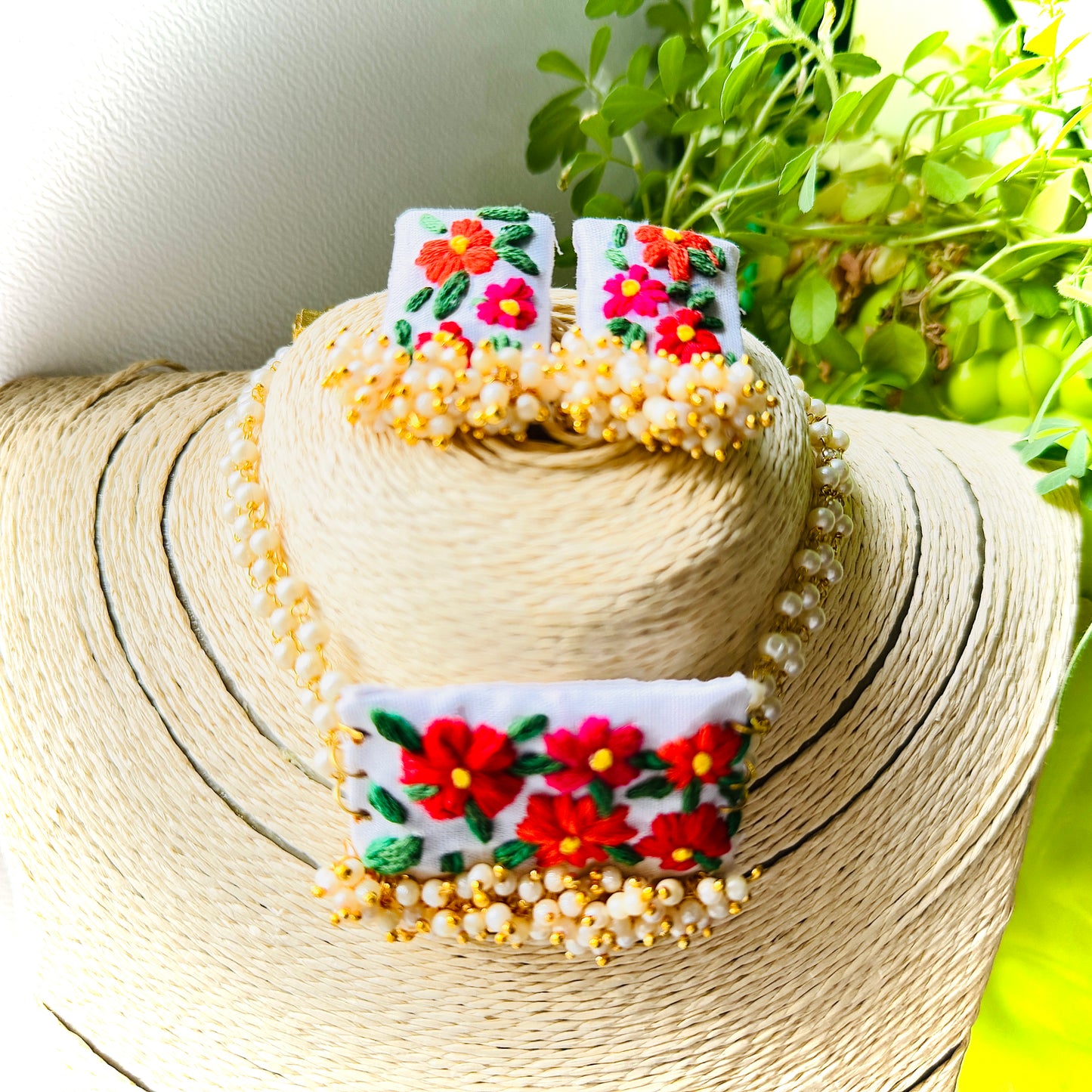 Decorative hat with floral embroidery and beads, placed on a straw hat with green plants in the background.