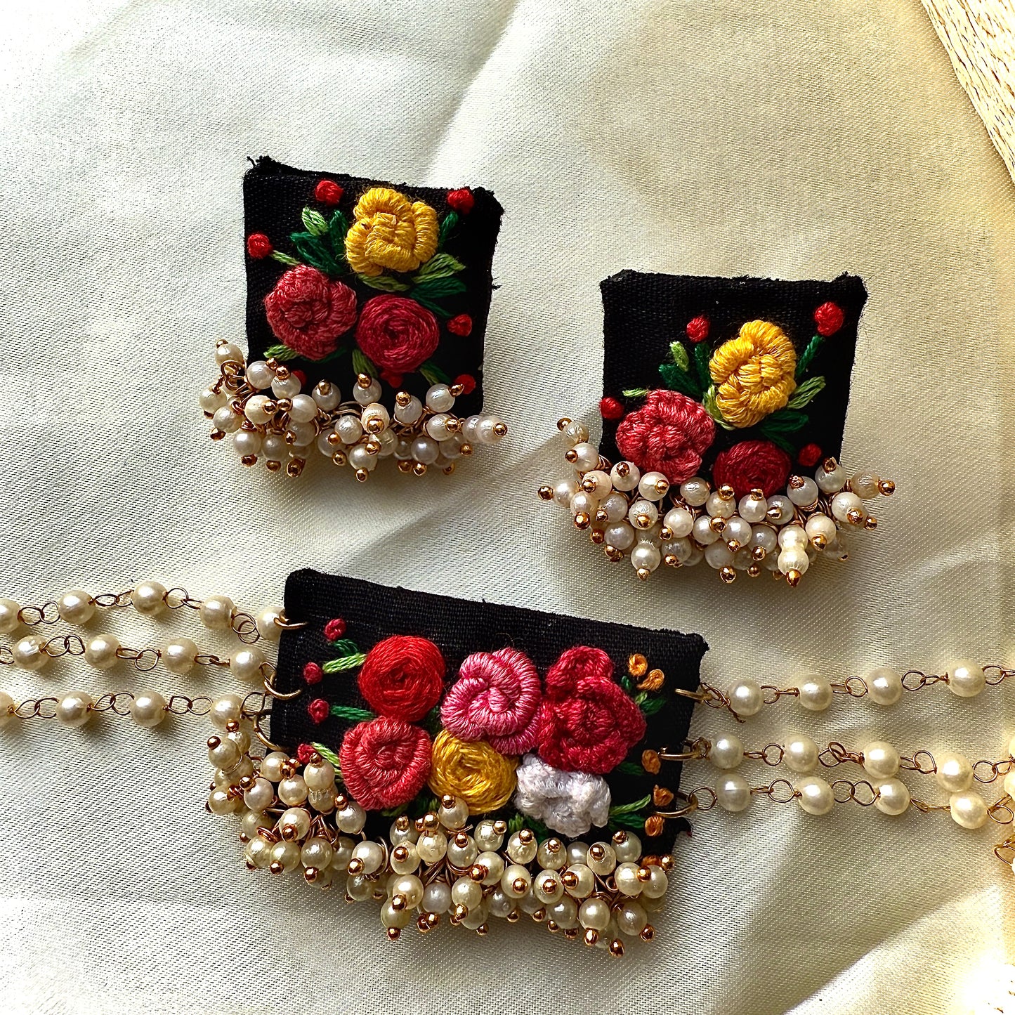 Embroidered floral brooches with pearl accents on a light fabric background